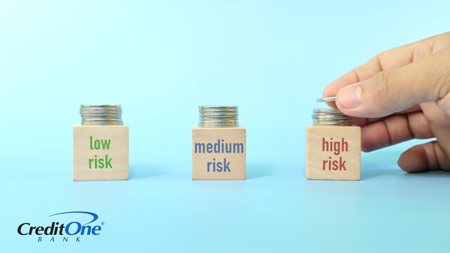 A hand stacks coins on three separate blocks marked “low risk,” “medium risk” and “high risk” to represent portfolio diversification.
