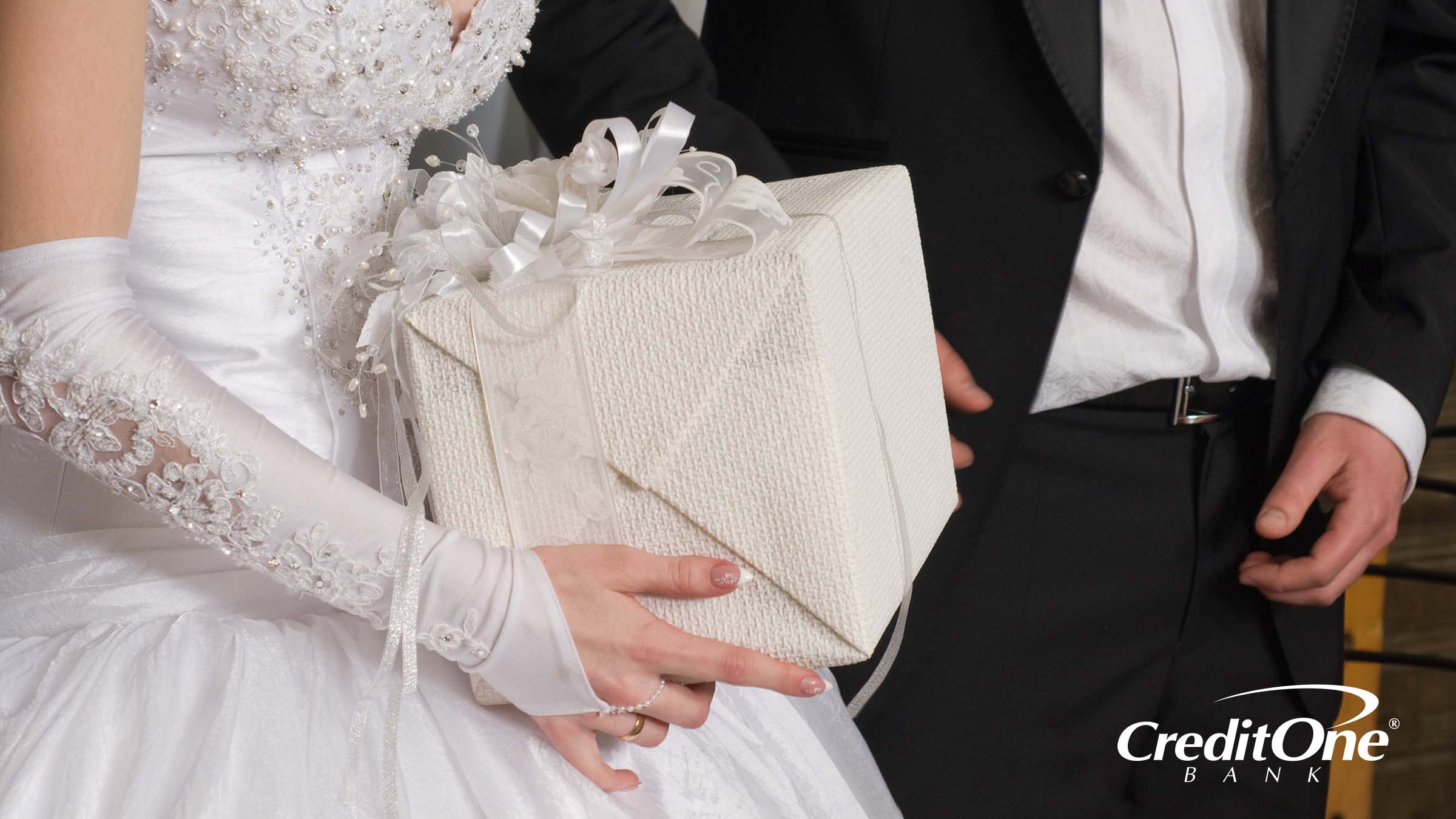 This photo of a bride and groom, shown from the shoulders down, reveals the bride holding a wrapped wedding gift, but we don’t know how much the gift giver spent.