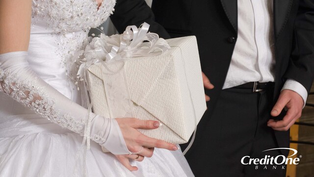 This photo of a bride and groom, shown from the shoulders down, reveals the bride holding a wrapped wedding gift, but we don’t know how much the gift giver spent.