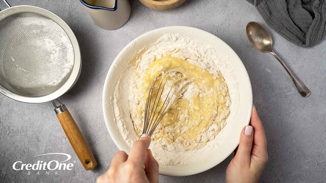 A mixing bowl with wet and dry ingredients is shown from above as the cook whisks the contents together, representing the concept of credit mix.