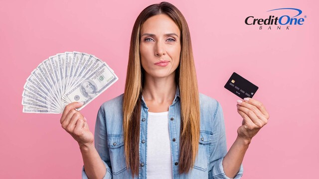 A woman holds up several $100 bills in her right hand and a credit card in her left, with a indecisive expression. Perhaps she is currently deciding whether cash or card is better.